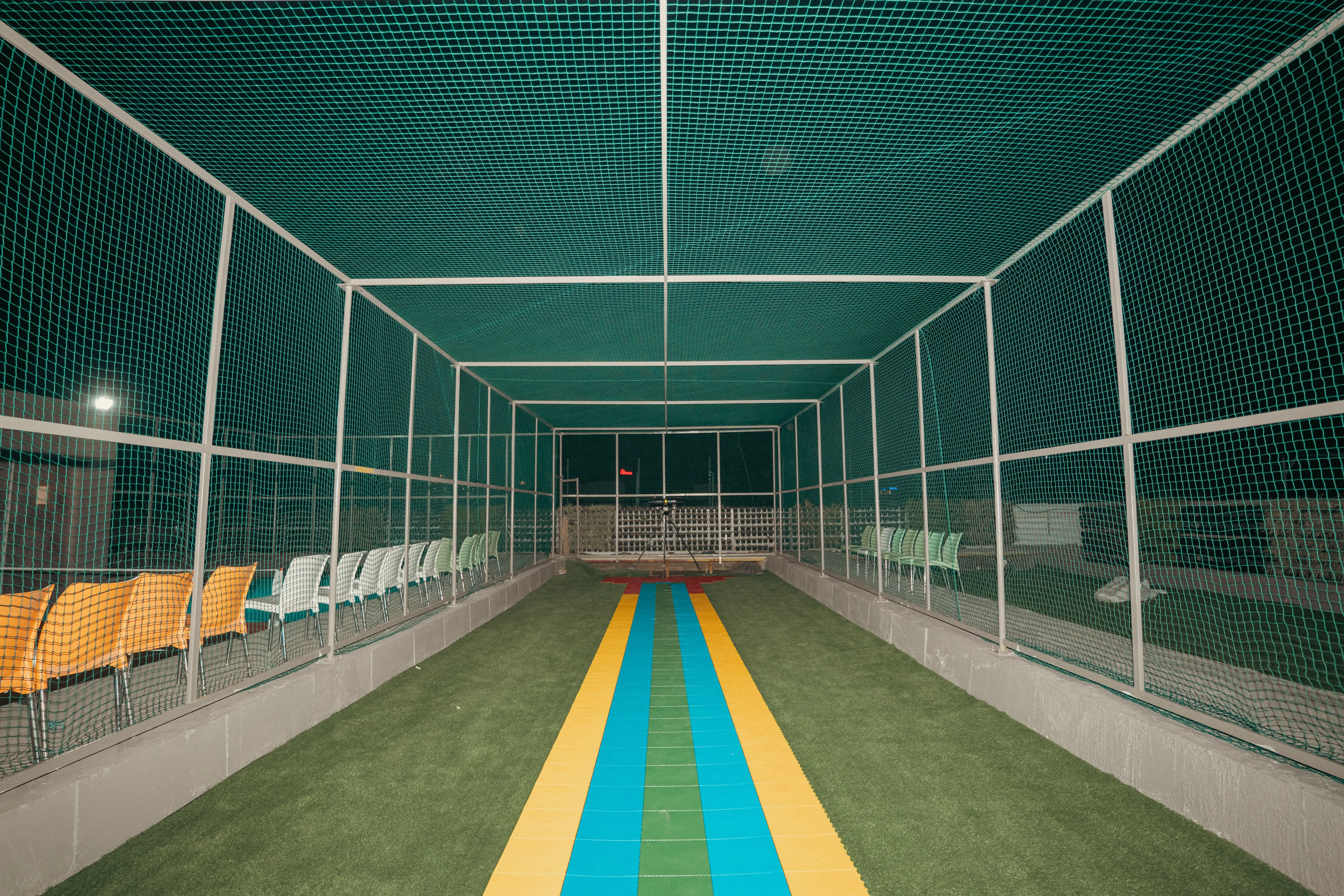 Dynamic action shot of players playing box cricket indoors with bright lights and enthusiastic crowd